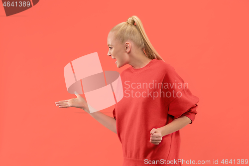 Image of Beautiful female half-length portrait isolated on coral studio backgroud. The young emotional surprised woman