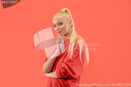 Image of The young woman whispering a secret behind her hand over coral background