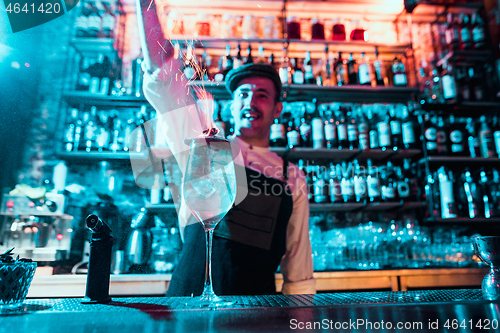 Image of Glass of fiery cocktail on the bar counter against the background of bartenders hands with fire