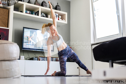 Image of Attractive sporty woman working out at home, doing pilates exercise in front of television in her living room. Social distancing. Stay healthy and stay at home during corona virus pandemic