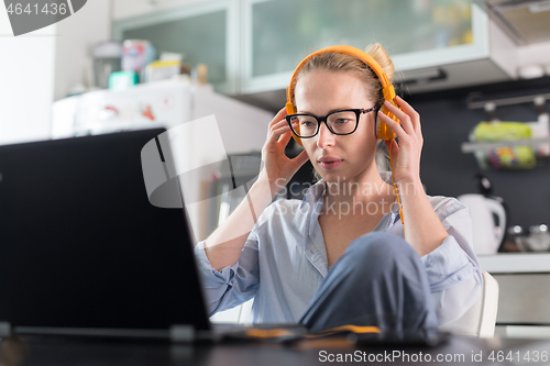 Image of Female freelancer in her casual home clothing working remotly from her dining table in the morning. Home kitchen in the background.