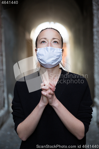 Image of Coronavirus outbreak. Young caucasian woman wearing medical protection face mask praying over coronavirus global pandemic, for salvation of humanity, health, anxiety and depression reduction