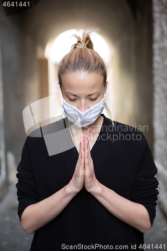 Image of Coronavirus outbreak. Young caucasian woman wearing medical protection face mask praying over coronavirus global pandemic, for salvation of humanity, health, anxiety and depression reduction