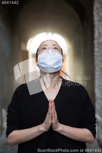 Image of Coronavirus outbreak. Young caucasian woman wearing medical protection face mask praying over coronavirus global pandemic, for salvation of humanity, health, anxiety and depression reduction