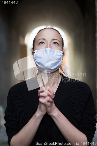 Image of Coronavirus outbreak. Young caucasian woman wearing medical protection face mask praying over coronavirus global pandemic, for salvation of humanity, health, anxiety and depression reduction