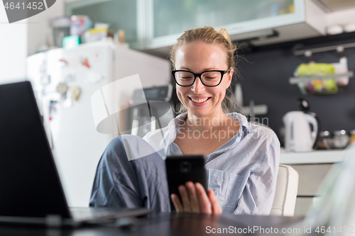 Image of Stay at home and social distancing. Woman in her casual home clothing working remotly from kitchen dining table. Video chatting using social media with friend, family, business clients or partners