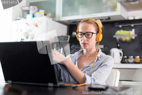 Image of Female freelancer in her casual home clothing working remotly from her dining table in the morning. Home kitchen in the background.