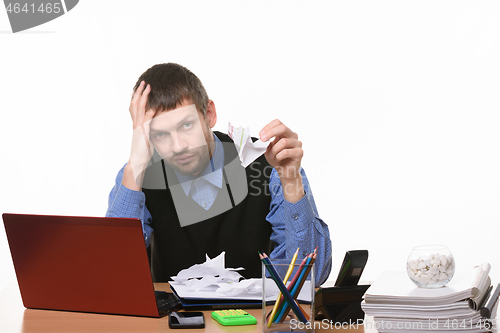 Image of fellow sits leaning his head on his arm with crumpled sheets of paper on the table and in his other hand