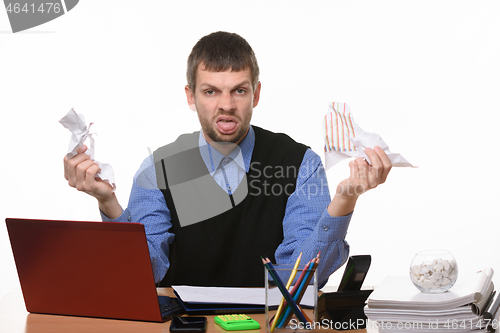 Image of Man at work desk holds crumpled sheets of paper and shows tongue