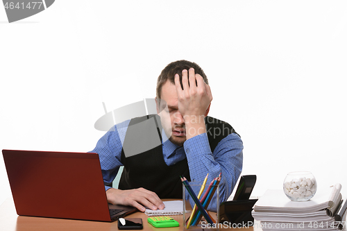 Image of tired and exhausted office employee rests his head on his hand sitting at the table