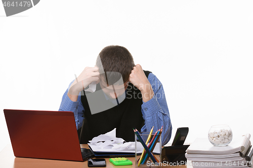 Image of employee sits clasping his head with his fists at the office table