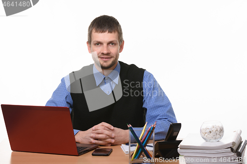 Image of An office worker sits at a table clutching his fingers and looks into the frame