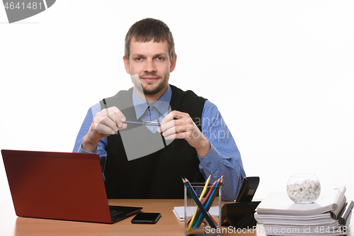 Image of a man sits at an office table and holds a pen on a white background