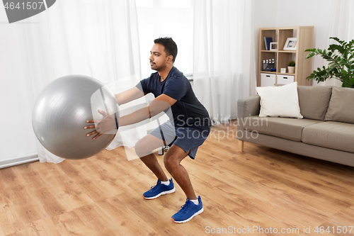 Image of man exercising and doing squats with ball at home
