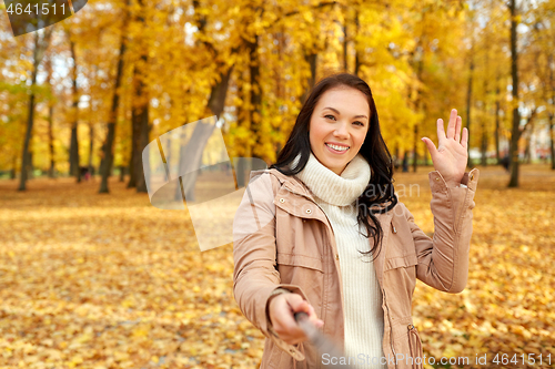 Image of woman taking picture by selfiestick at autumn park