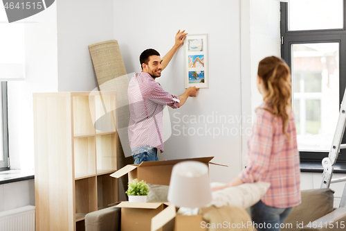 Image of happy couple moving to new home and hanging photo