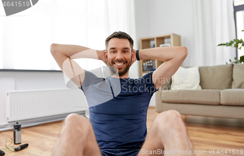 Image of smiling man making abdominal exercises at home