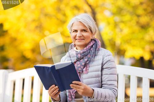 Image of happy senior woman reading book at autumn park