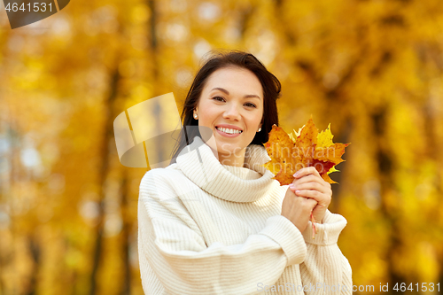 Image of happy young woman with maple leaves in autumn park