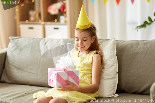 Image of happy girl in party hat with birthday gift at home