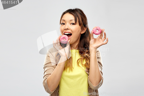 Image of happy asian woman eating donuts