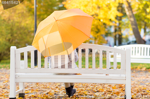 Image of woman with umbrella sits on bench in autumn park