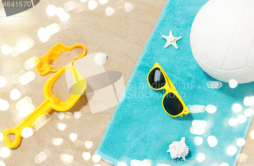 Image of sunglasses, sand toys and ball on beach towel