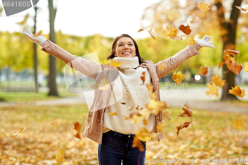 Image of happy woman having fun with leaves in autumn park