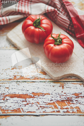 Image of Top view of a white cutting board with a fresh juicy tomatoes on a wooden table
