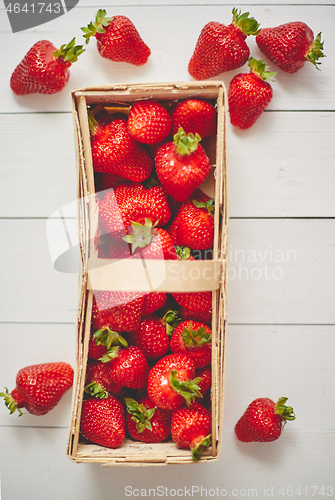 Image of Wooden container with fresh red strawberries. Placed on white table.