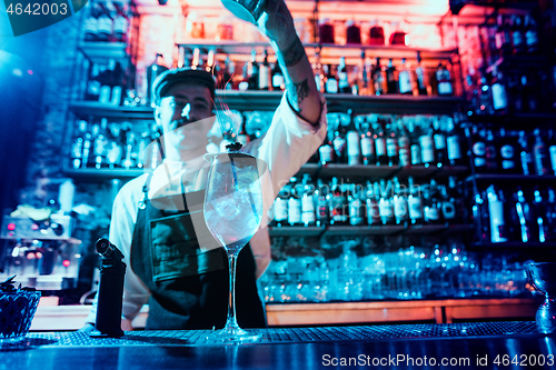 Image of Glass of fiery cocktail on the bar counter against the background of bartenders hands with fire