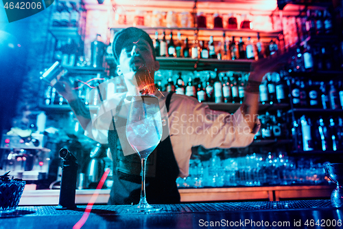 Image of Glass of fiery cocktail on the bar counter against the background of bartenders hands with fire