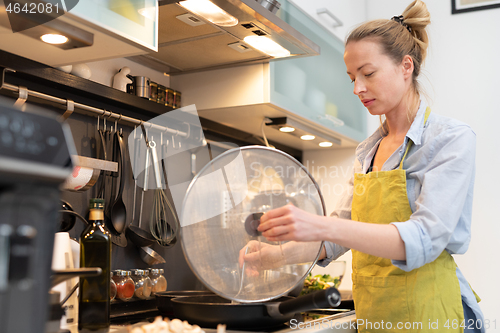 Image of Stay at home housewife woman cooking in kitchen, stir frying dish in a saucepan, preparing food for family dinner.