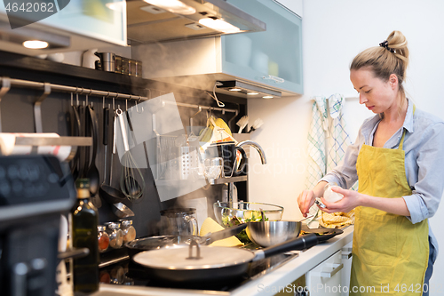 Image of Stay at home housewife woman cooking in kitchen, salting dish in a saucepan, preparing food for family dinner.