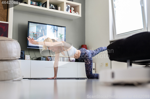 Image of Attractive sporty woman working out at home, doing pilates exercise in front of television in her living room. Social distancing. Stay healthy and stay at home during corona virus pandemic