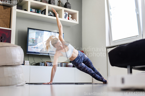 Image of Attractive sporty woman working out at home, doing pilates exercise in front of television in her living room. Social distancing. Stay healthy and stay at home during corona virus pandemic