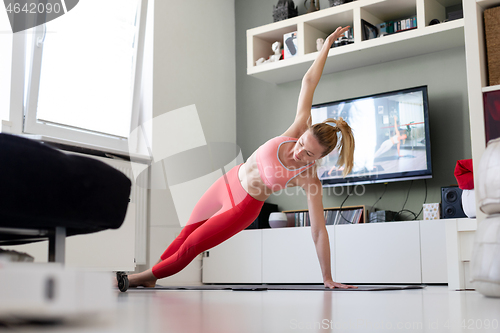 Image of Attractive sporty woman working out at home, doing pilates exercise in front of television in her living room. Social distancing. Stay healthy and stay at home during corona virus pandemic