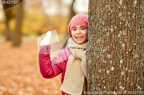 Image of happy girl peeking out tree in autumn park