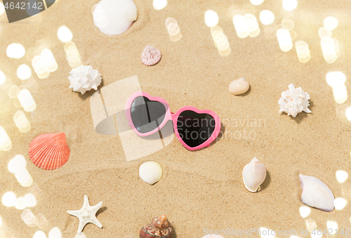 Image of heart-shaped sunglasses and shells on beach sand