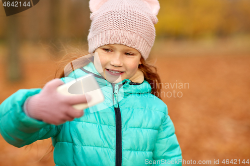 Image of girl taking selfie by smartphone at autumn park
