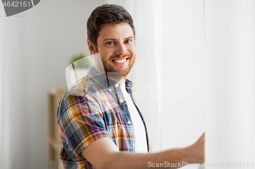 Image of young man opening window curtain at home