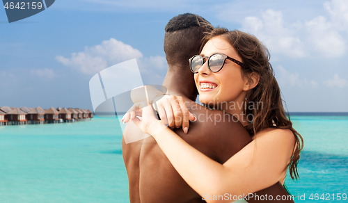 Image of happy mixed race couple hugging on beach