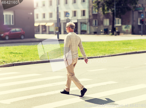 Image of senior man walking along city crosswalk