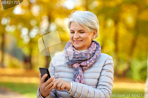 Image of happy senior woman with smartphone at autumn park