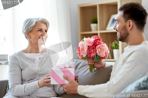 Image of son giving present and flowers to senior mother