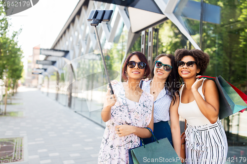 Image of women with shopping bags taking selfie outdoors