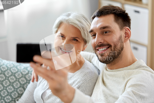 Image of senior mother with adult son taking selfie at home