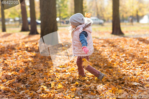 Image of happy girl playing with leaves at autumn park