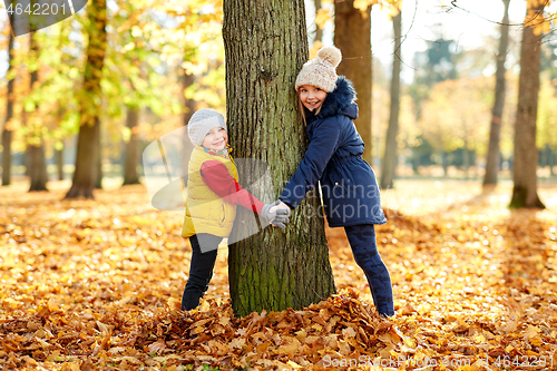 Image of happy children at tree trunk in autumn park