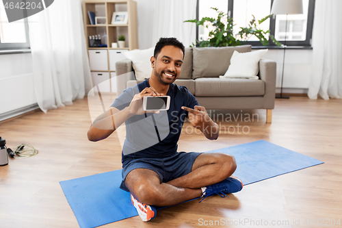 Image of indian man with smartphone on exercise mat at home